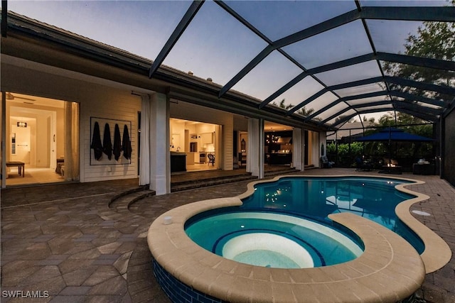 pool at dusk featuring a pool with connected hot tub and a patio