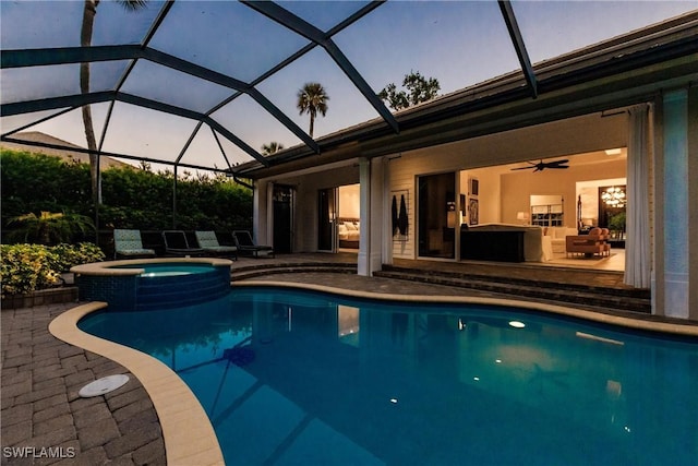 pool at dusk featuring a pool with connected hot tub, a lanai, ceiling fan, and a patio