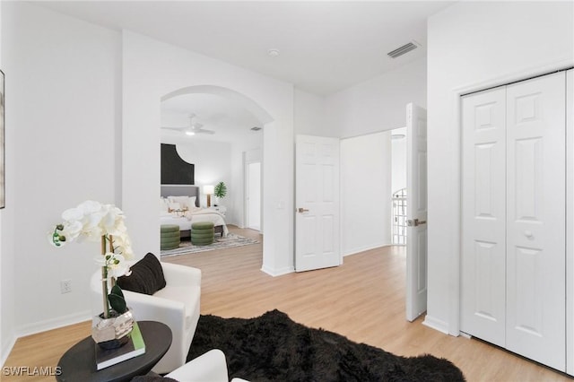 interior space with ceiling fan, arched walkways, light wood finished floors, and visible vents