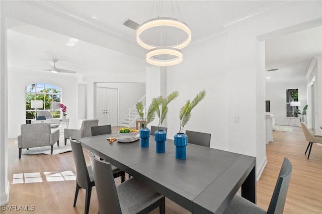 dining space with light wood-style floors, crown molding, stairway, and visible vents