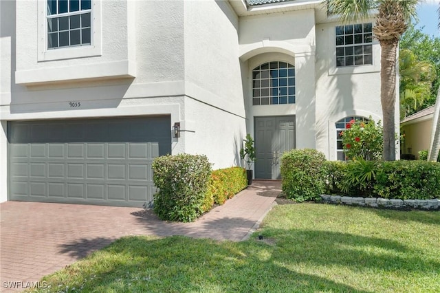 view of exterior entry with stucco siding, a garage, a yard, and decorative driveway
