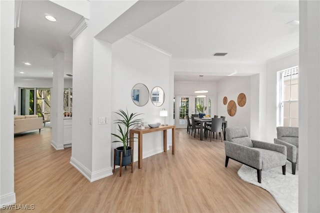 hallway featuring light wood-style flooring, ornamental molding, baseboards, and visible vents