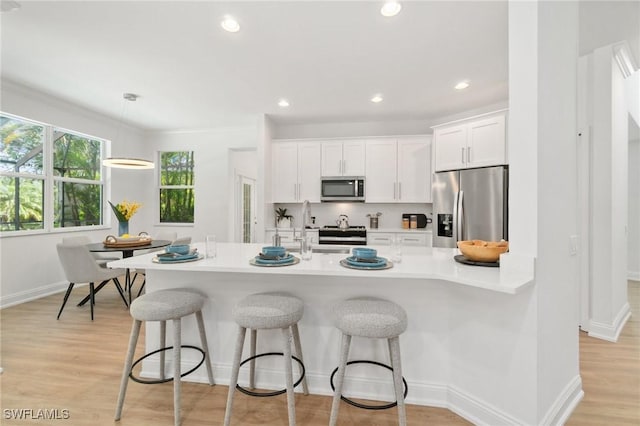 kitchen with light countertops, a kitchen bar, light wood-style flooring, stainless steel appliances, and white cabinets
