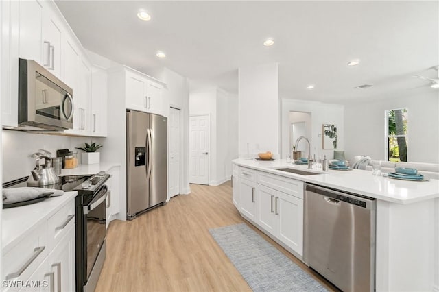 kitchen with white cabinetry, open floor plan, light countertops, a sink, and appliances with stainless steel finishes