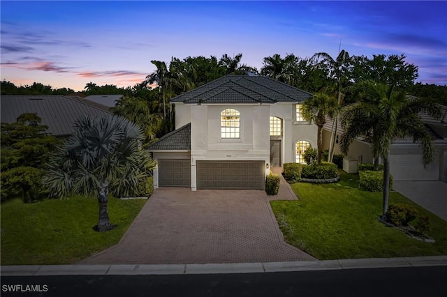 view of front of house featuring an attached garage, stucco siding, a front yard, a tile roof, and driveway