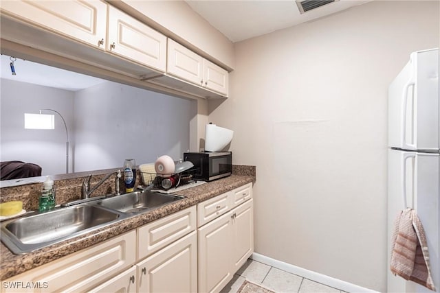 kitchen with light tile patterned flooring, visible vents, white cabinetry, a sink, and freestanding refrigerator