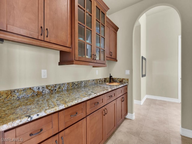 866 Cal Cove Dr, Fort Myers, FL 33919 - kitchen featuring arched walkways, light stone countertops, brown cabinets, and baseboards