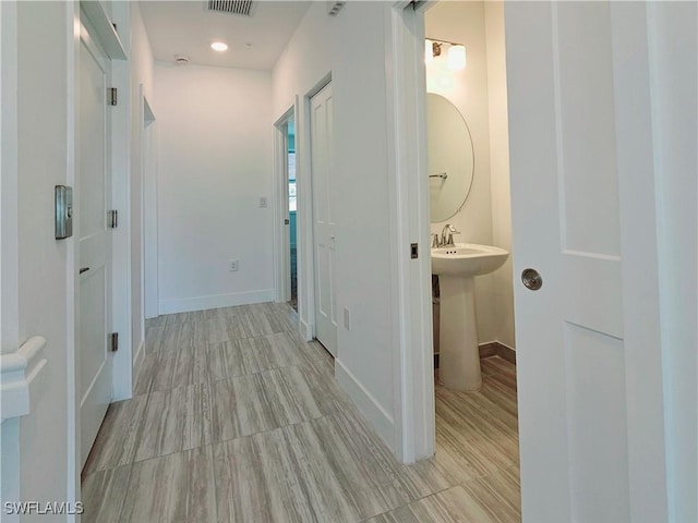 hall featuring a sink, baseboards, and visible vents