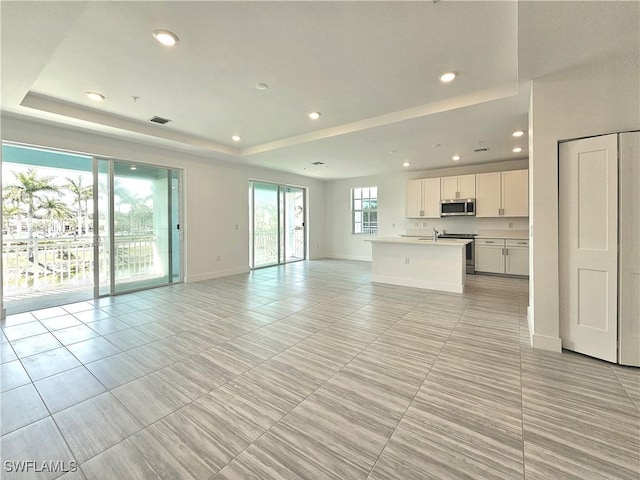 unfurnished living room with a tray ceiling, baseboards, visible vents, and recessed lighting