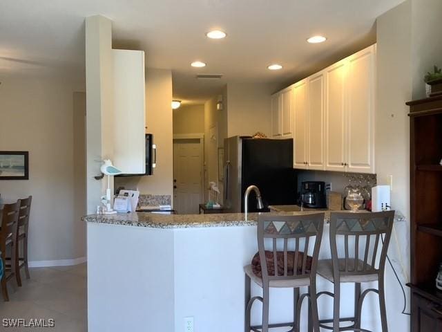 11735 Eros Rd, Lehigh Acres, FL 33971 - kitchen featuring white cabinetry, stove, light stone counters, freestanding refrigerator, and a peninsula
