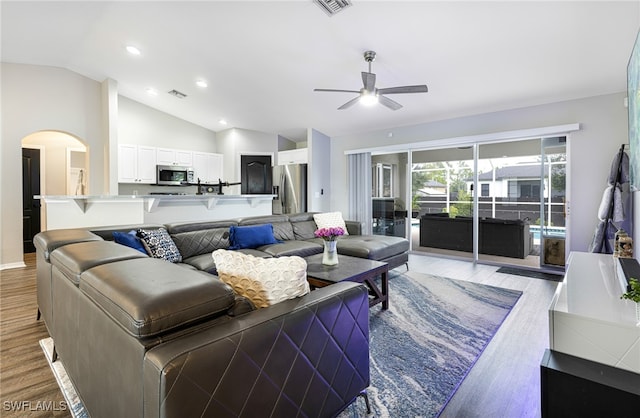 living area featuring arched walkways, light wood-style flooring, a ceiling fan, lofted ceiling, and visible vents