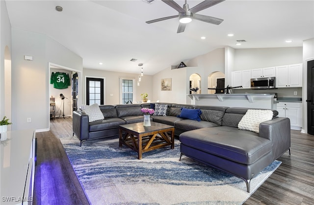 living area with arched walkways, ceiling fan, vaulted ceiling, and dark wood-type flooring