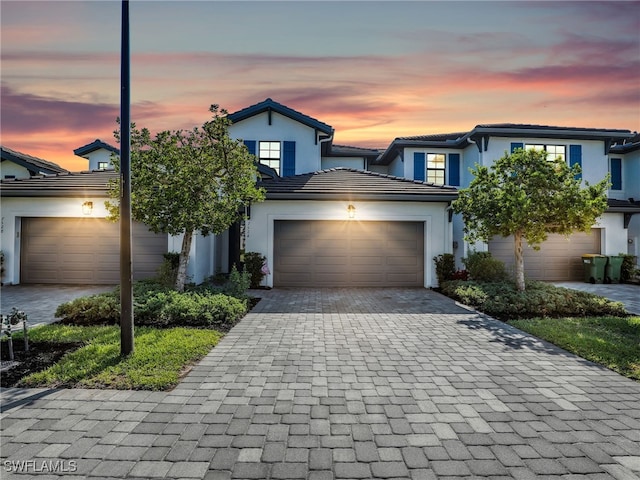 view of front of home with a garage, a tile roof, stucco siding, and decorative driveway