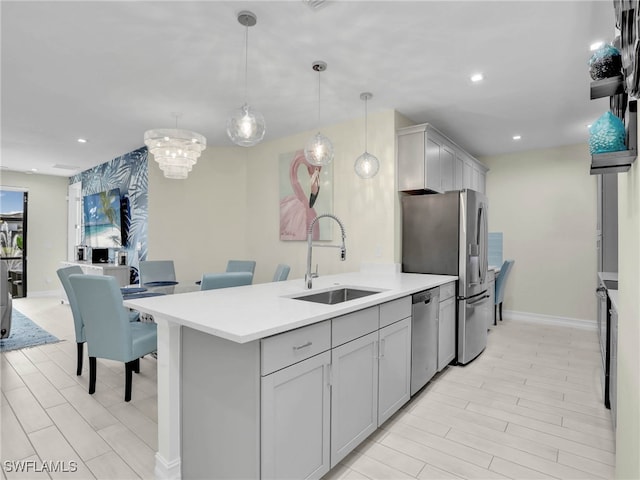 kitchen with gray cabinetry, stainless steel appliances, light countertops, and a sink
