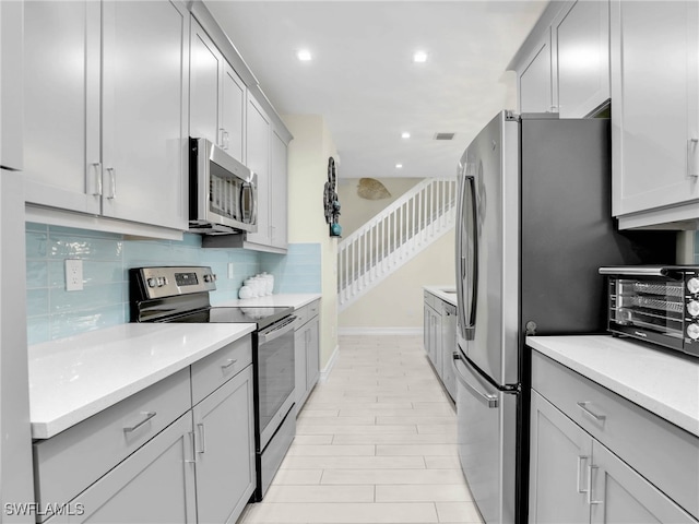 kitchen with stainless steel appliances, backsplash, baseboards, a toaster, and gray cabinetry