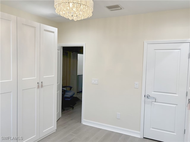 unfurnished bedroom with an inviting chandelier, a closet, visible vents, light wood-style flooring, and baseboards