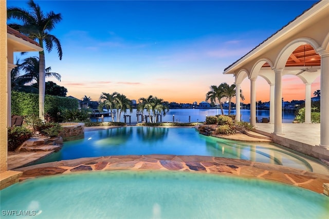 580 S Heathwood Dr, Marco Island, FL 34145 - pool at dusk featuring a pool with connected hot tub, a water view, and ceiling fan