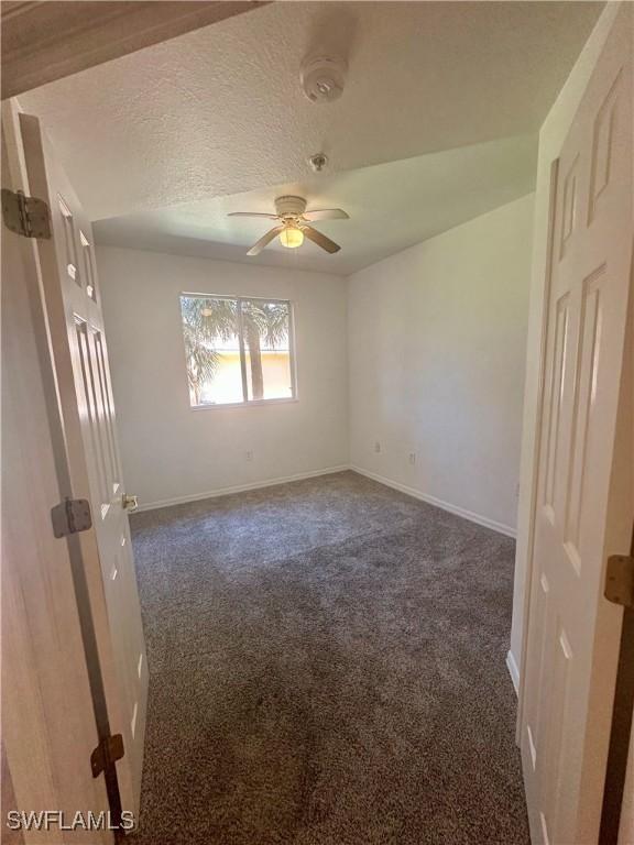 unfurnished room featuring baseboards, ceiling fan, dark carpet, and a textured ceiling