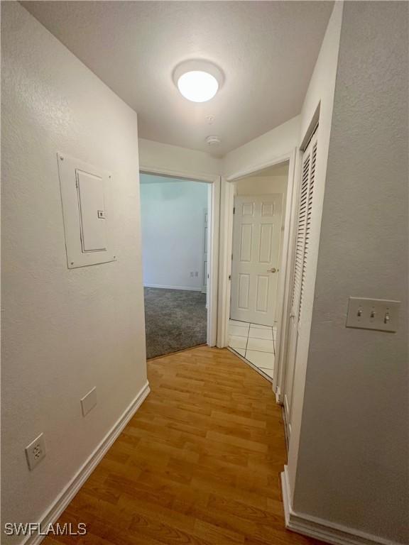 hallway featuring electric panel, baseboards, and wood finished floors