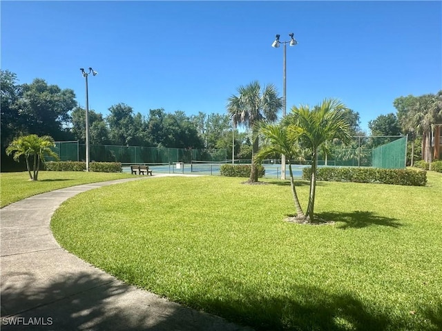 view of property's community with a tennis court, fence, and a yard