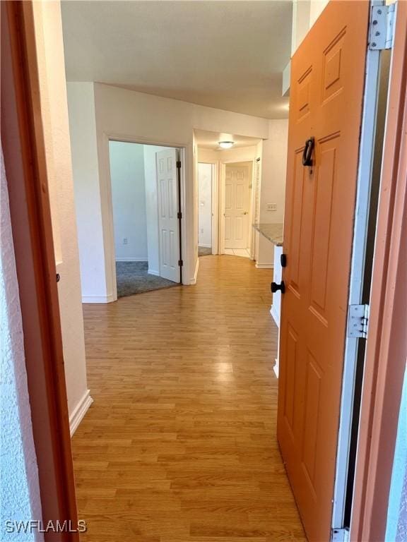 corridor with light wood-style flooring and baseboards