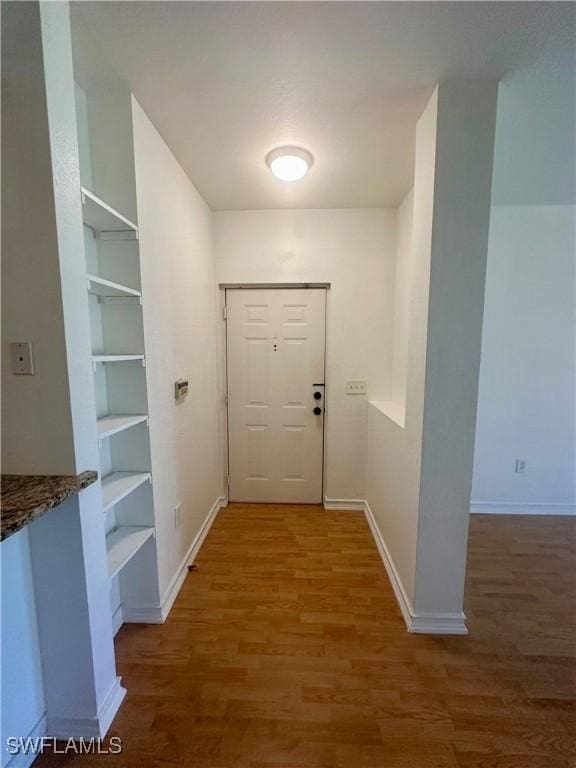 hallway featuring baseboards, wood finished floors, and built in features