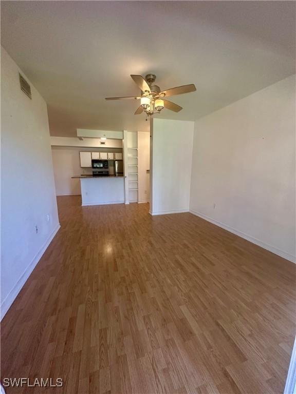 unfurnished living room with baseboards, visible vents, wood finished floors, and a ceiling fan