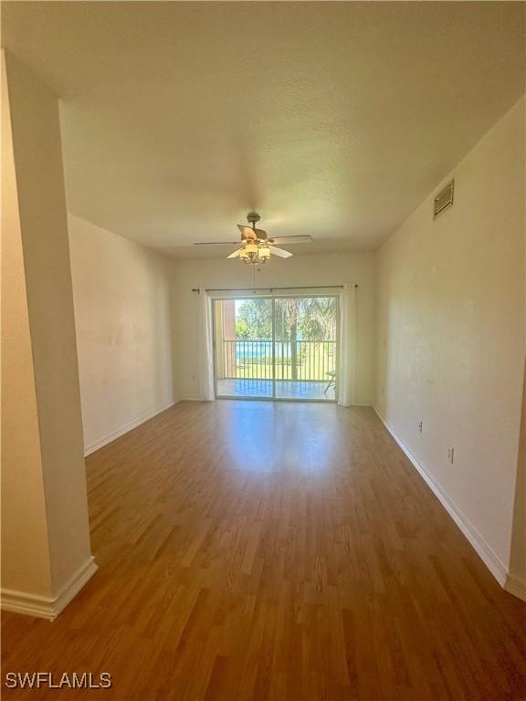 spare room featuring a ceiling fan, visible vents, baseboards, and wood finished floors
