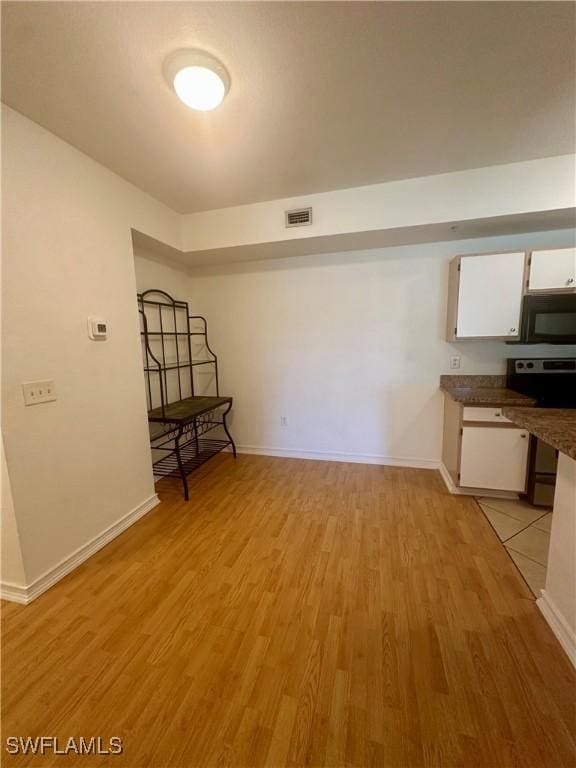 interior space featuring light wood-type flooring, stainless steel electric range oven, visible vents, white cabinets, and black microwave