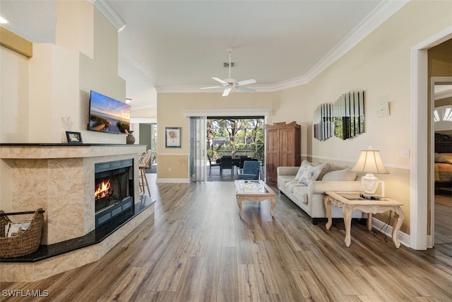 living room featuring a tiled fireplace, wood finished floors, ornamental molding, and a ceiling fan
