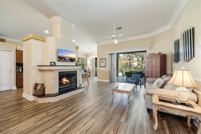 living area featuring a ceiling fan, wood finished floors, a premium fireplace, and crown molding