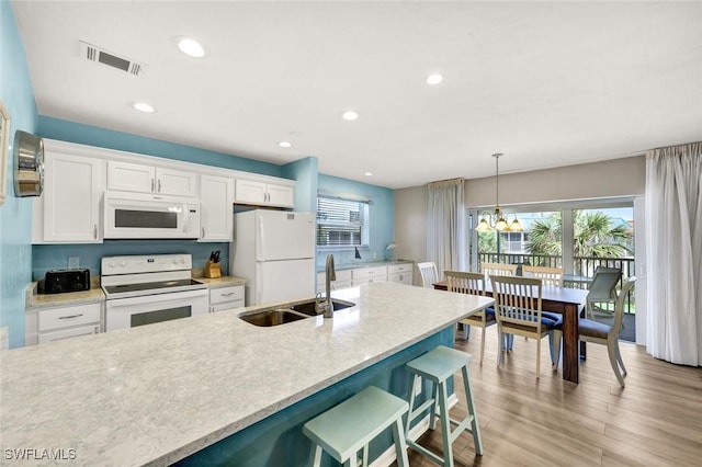 kitchen with a sink, white cabinetry, a breakfast bar, white appliances, and light wood-style floors