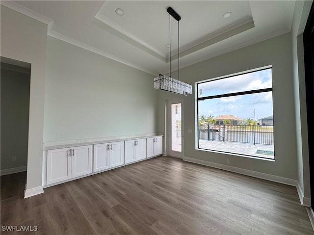 unfurnished dining area featuring dark wood-style floors, ornamental molding, and a raised ceiling
