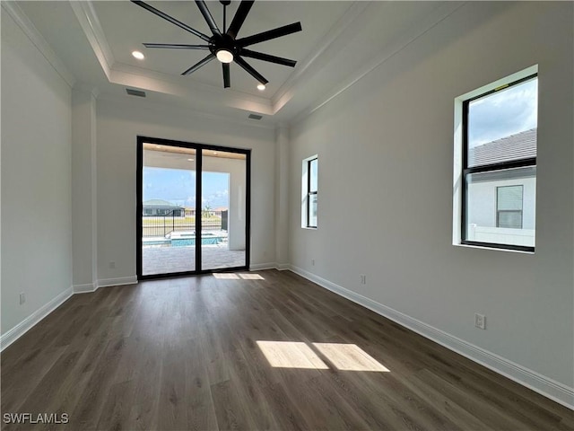 spare room featuring a raised ceiling, dark wood-style flooring, baseboards, and ornamental molding