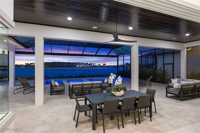 patio terrace at dusk featuring glass enclosure, an outdoor pool, an outdoor living space, outdoor dining space, and a water view