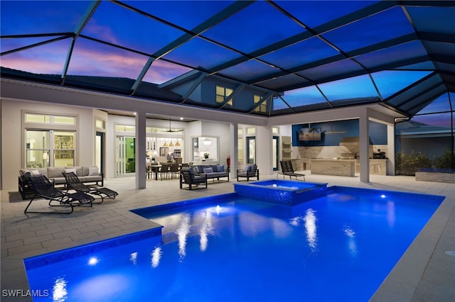 pool at dusk with an outdoor kitchen, ceiling fan, a pool with connected hot tub, an outdoor hangout area, and a patio area