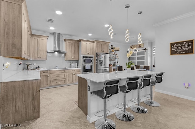 kitchen featuring light countertops, crown molding, stainless steel appliances, wall chimney range hood, and a kitchen breakfast bar