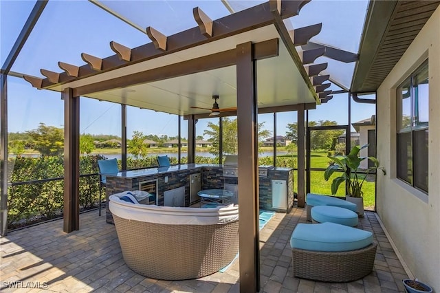 view of patio with glass enclosure, a water view, and an outdoor kitchen