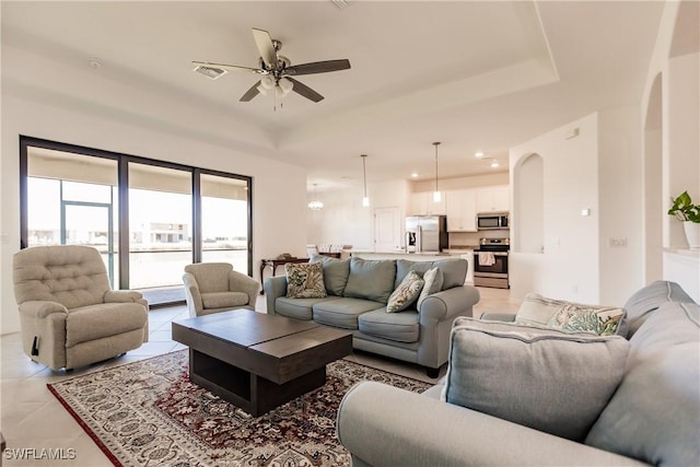 living room with light tile patterned floors, a raised ceiling, arched walkways, visible vents, and ceiling fan