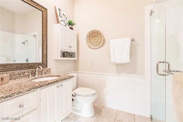 bathroom with toilet, wainscoting, tile walls, a shower stall, and vanity