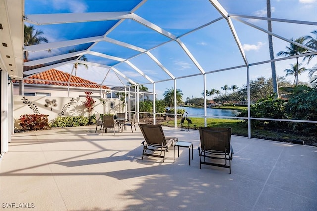 view of patio / terrace featuring glass enclosure, outdoor dining space, and a water view