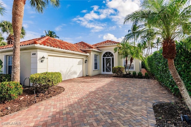 mediterranean / spanish-style house with stucco siding, decorative driveway, a tiled roof, and a garage