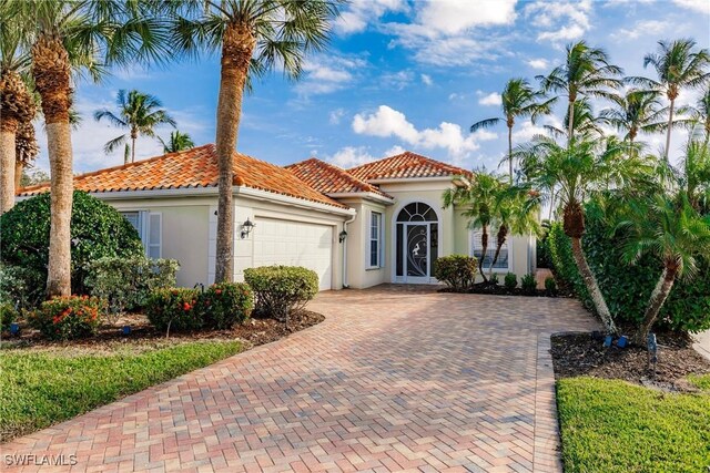 mediterranean / spanish-style house with an attached garage, a tiled roof, stucco siding, and decorative driveway