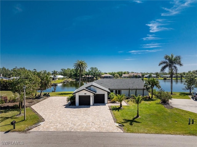 view of front of house with a water view, decorative driveway, a garage, a front lawn, and stucco siding