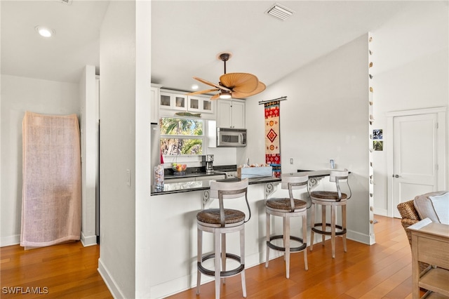 5773 Sanibel Captiva Rd, Sanibel, FL 33957 - kitchen featuring stainless steel microwave, a kitchen breakfast bar, visible vents, and wood finished floors