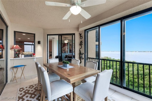 dining space with a ceiling fan, light tile patterned flooring, a water view, and a textured ceiling