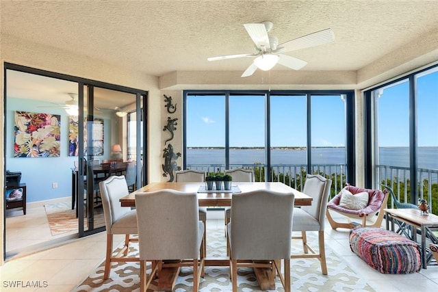 dining area featuring light tile patterned floors, a water view, a textured ceiling, and a ceiling fan