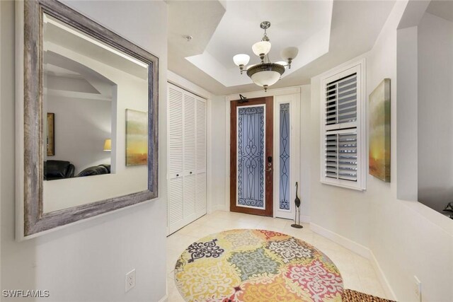 tiled entrance foyer with baseboards, a tray ceiling, and a chandelier