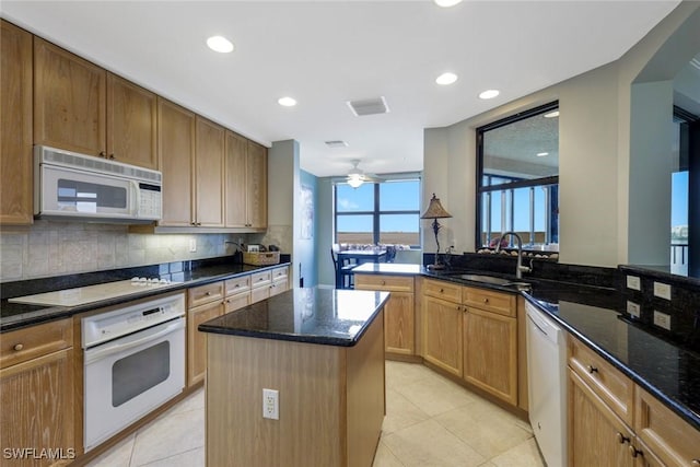 kitchen with light tile patterned floors, a sink, dark stone countertops, and white appliances