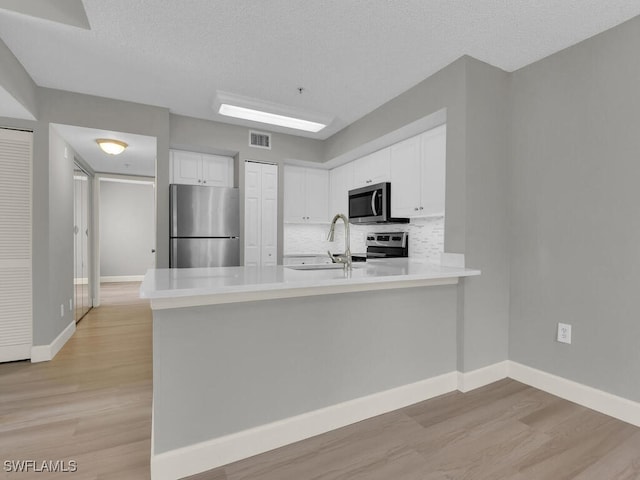 1180 Wildwood Lakes Blvd Unit 207, Naples, FL 34104 - kitchen featuring light wood-style flooring, a peninsula, white cabinetry, a sink, and stainless steel appliances